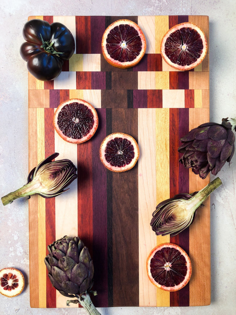 Large exotic wood cutting board with blood oranges and purple artichokes